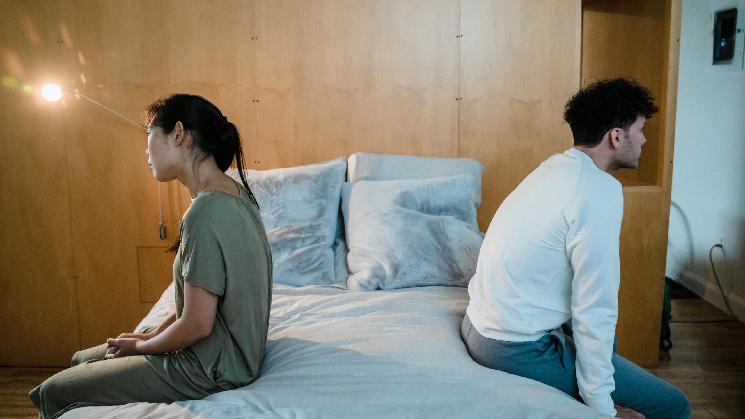 A couple sits back to back on a bed, showing tension due to sex and porn addiction and betrayal trauma.