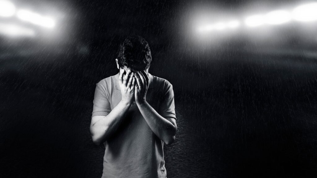 Black and white image of a man alone in the rain with his face buried in his hands, conveying emotional pain, isolation, and silent struggle — representing the hidden burden many men carry with their mental health